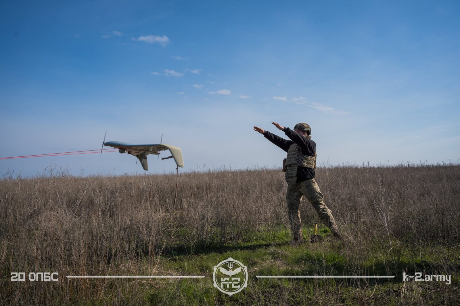 Військовий запускає безпілотник літакового типу з відкритої польової ділянки під ясним небом. Кадр передає момент роботи операторів БПЛА, коли апарат уже набирає політ над сухою травою.