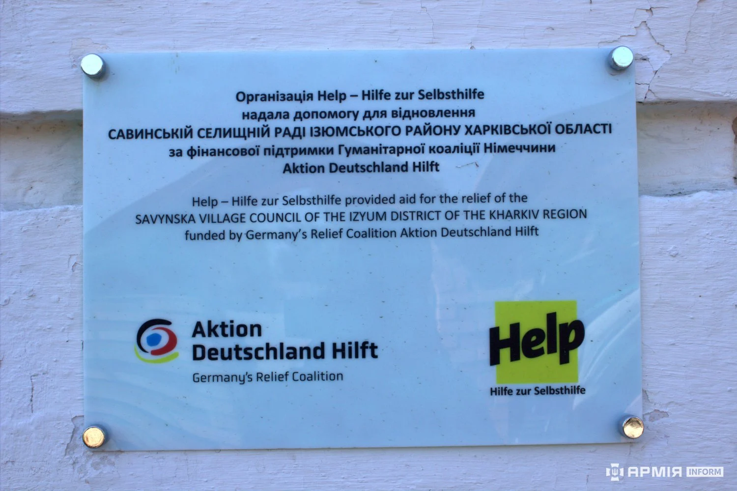 Інформаційна табличка повідомляє про допомогу організації Help – Hilfe zur Selbsthilfe для відновлення Савинської селищної ради. На табличці також розміщені логотипи Help та Action Deutschland Hilft.