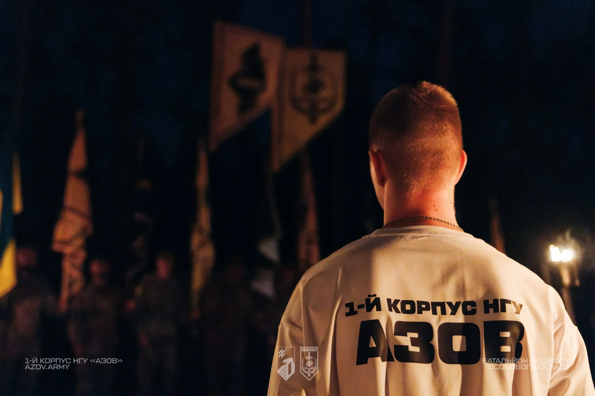 Чоловік у світлій футболці стоїть спиною до камери; на одязі великими літерами написано «1-й корпус НГУ АЗОВ».