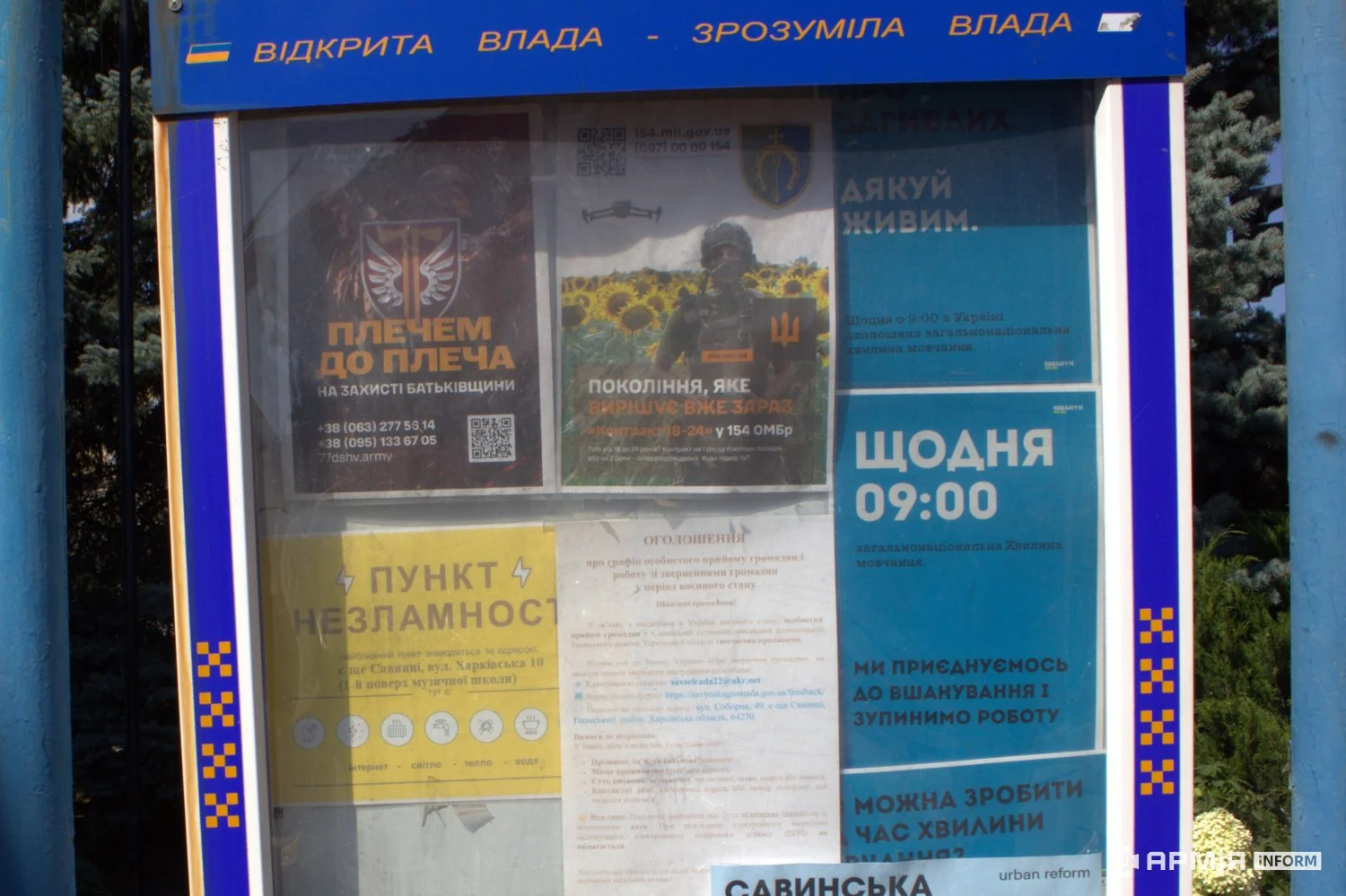 Інформаційний стенд заповнений оголошеннями та плакатами різної тематики. Серед них розміщені матеріали про пункт незламності, військову службу та загальнонаціональну хвилину мовчання о 09:00.
